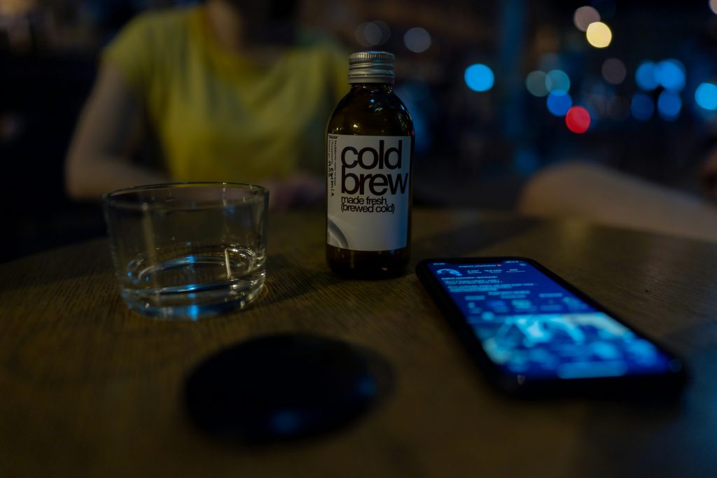 بطری کلد برو و موبایل و لیوان روی میز در کافه