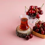 یک استکان چای آلبالو در کنار دو ظرف آلبالوی تازه