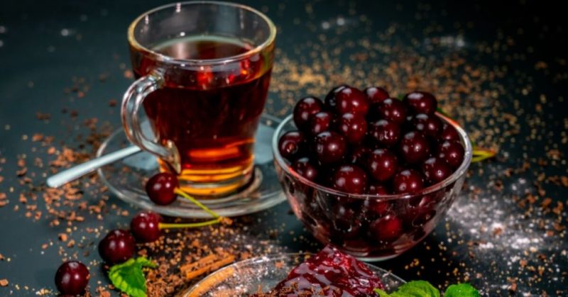 لیوان دمنوش میوه ای در کنار ظرف میوه