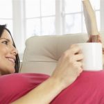 خانمی که باردار است و دراز کشیده در حال نوشیدن یک نوشیدنی گرم