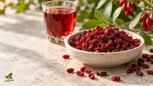 زرشک خشک در کاسهٔ سفالی کنار یک لیوان نوشیدنی زرشک