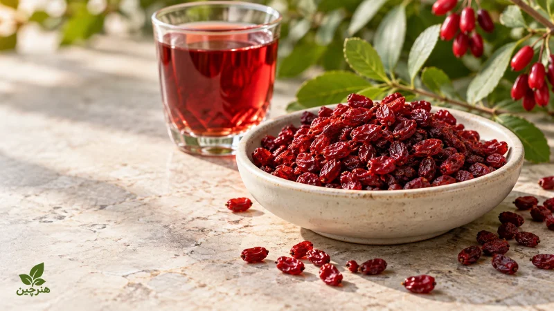 زرشک خشک در کاسهٔ سفالی کنار یک لیوان نوشیدنی زرشک