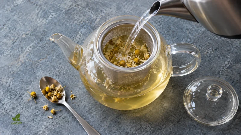 ریختن آب داغ روی گل خشک بابونه در صافی قوری شیشه‌ای