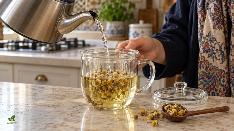 ریختن آب داغ روی گل بابونه در فنجان باز با درپوش کنار ظرف
