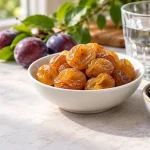 آلو بخارای زرد و آلوی خشک تیره کنار لیوان آب برای بررسی اثر بر یبوست