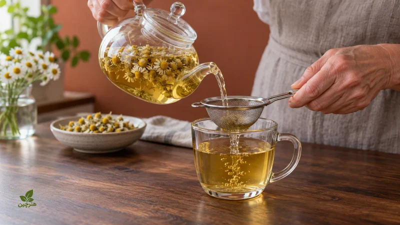 صاف‌کردن دمنوش بابونه از قوری شیشه‌ای داخل فنجان با صافی فلزی